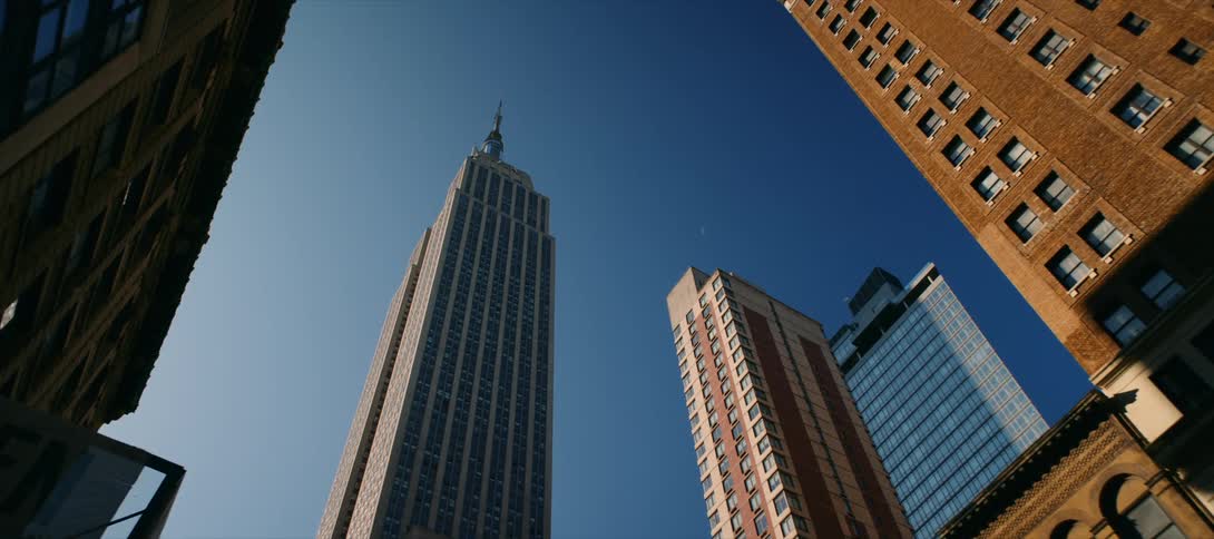 The video shows an upwardangle shot of the empire state building in new york city the camera pans from the bottom to the top of the skyscraper on a clear day other buildings are visible on both sides of the frame