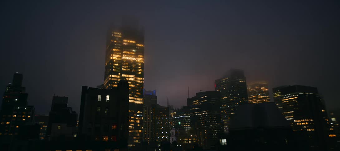 The lights of downtown skyscrapers glow through a thick layer of fog on a dark and atmospheric city night