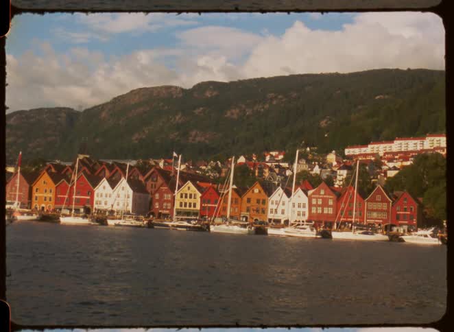 A coastal town on an island with a series of sailboats docked in the bay at midday surrounded by mountains