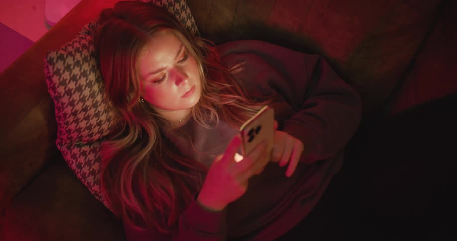 Woman lying on the couch looking at her cellphone under red lighting