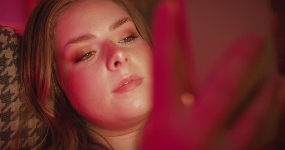 Woman lying down attentively looking at a cellphone screen under red lighting