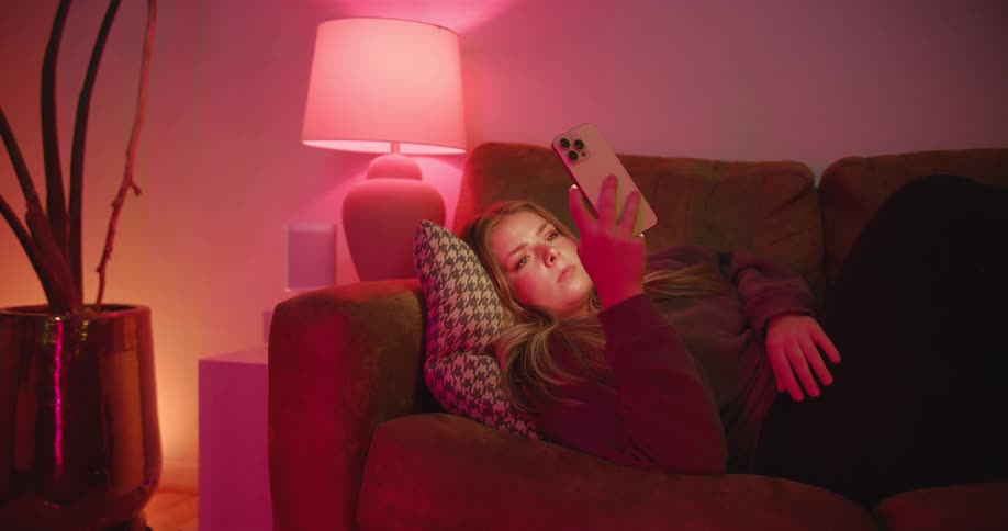 Woman lying on the couch using a cellphone in a room lit by red light