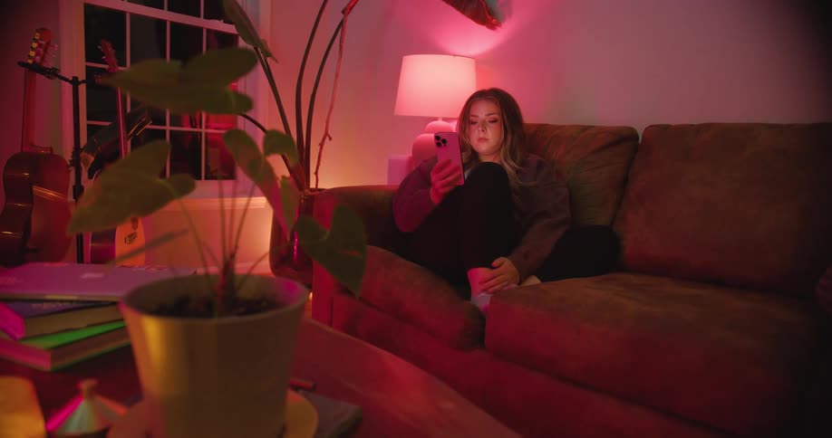 A young woman uses a mobile phone while sitting on a couch in a living room at night