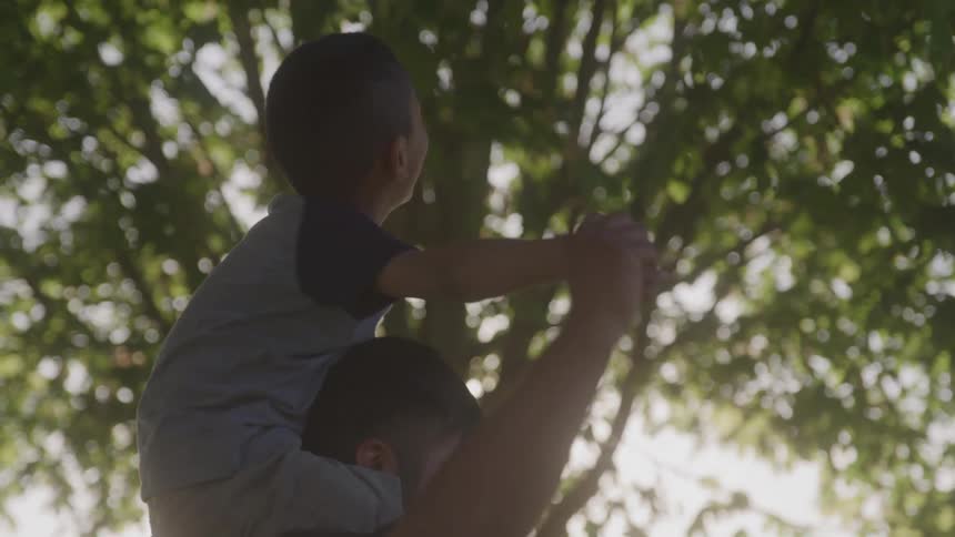 A smiling little boy is looking up while sitting on the shoulders of an adult man who is spinning around