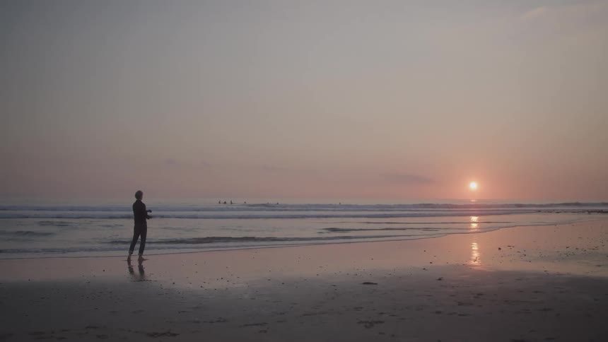 A man on the beach skips rocks into the ocean water at sunset