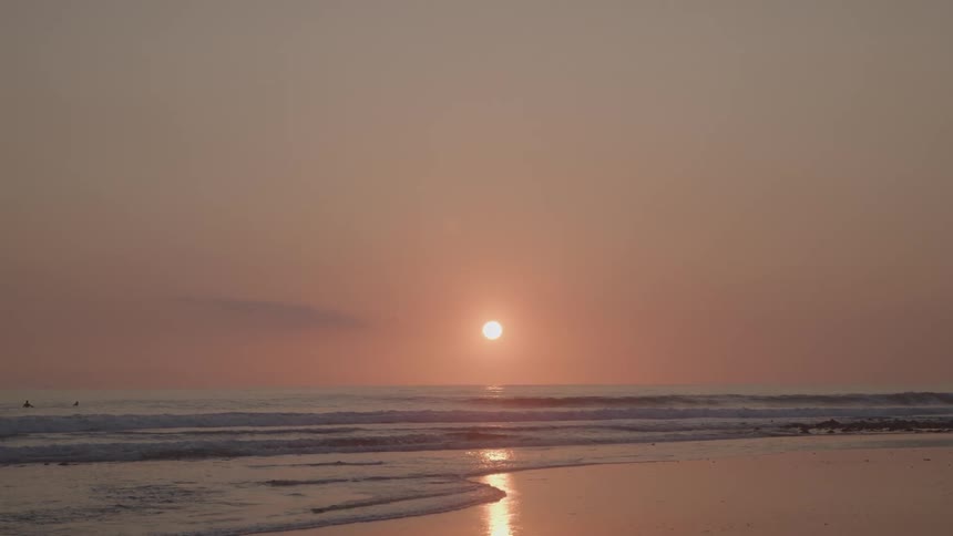 A serene sunset on a beach with the suns reflection shimmering on the gentle ocean waves as they lap at the sandy shore