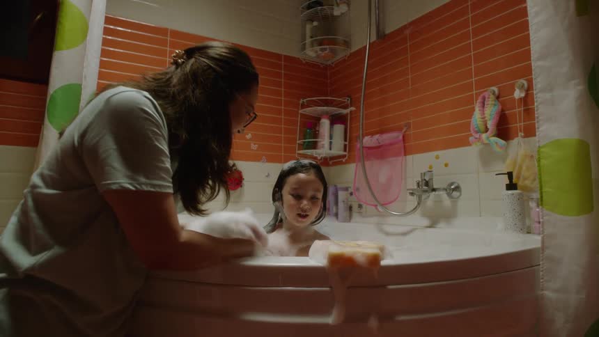 A mother helps her child take a bubble bath in the bathroom