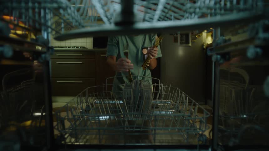 A boy loads utensils into a dishwasher in a kitchen