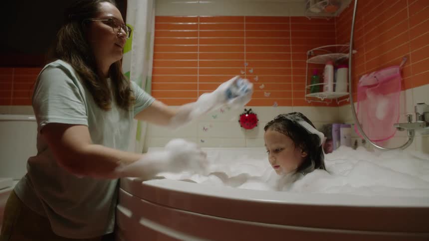 A mother helps her child take a bubble bath in the bathroom