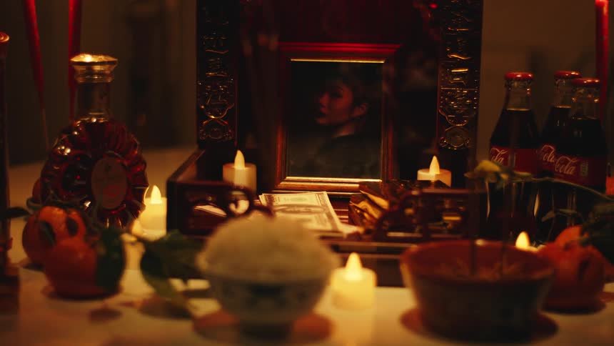 A candle lit altar holds a framed photo of a woman surrounded by offerings