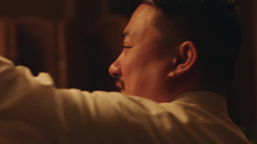 In a warm lowlight setting a man and a woman are seen in a closeup shot dancing and having a conversation