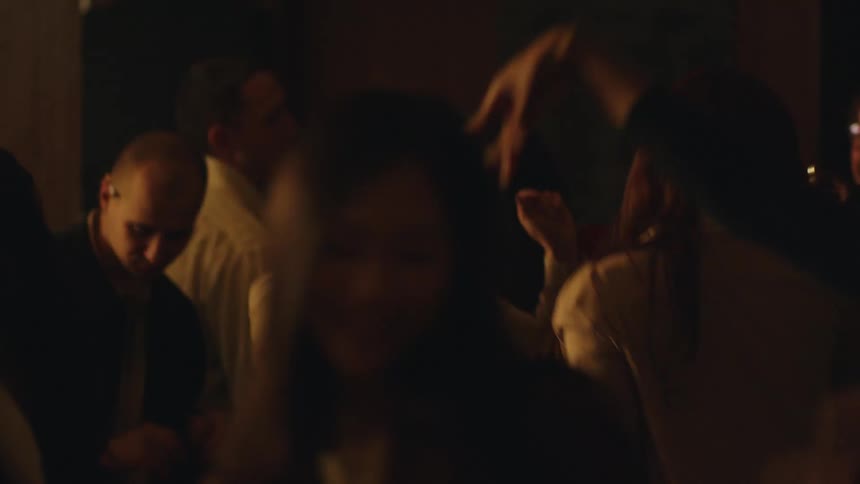 The video shows a group of people at a party or event in a dimly lit dark room the camera moves in a disoriented way and the people in the video can be seen dancing and socializing