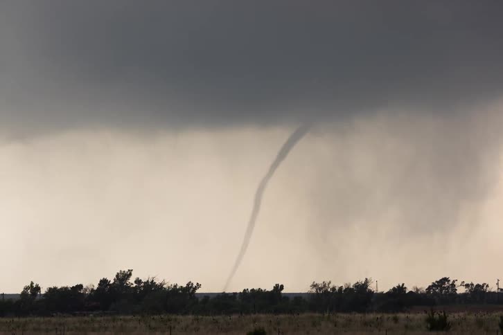 A tornado swirling across a grass field at sunset in a rural area