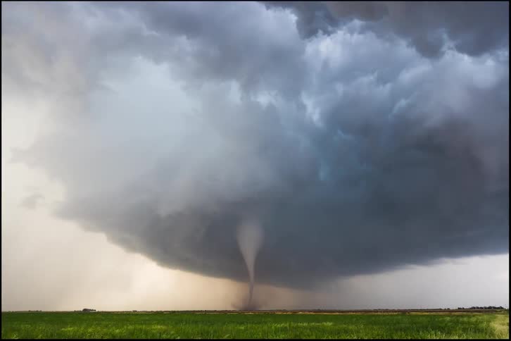 Storm clouds gather over a field forming a tornado