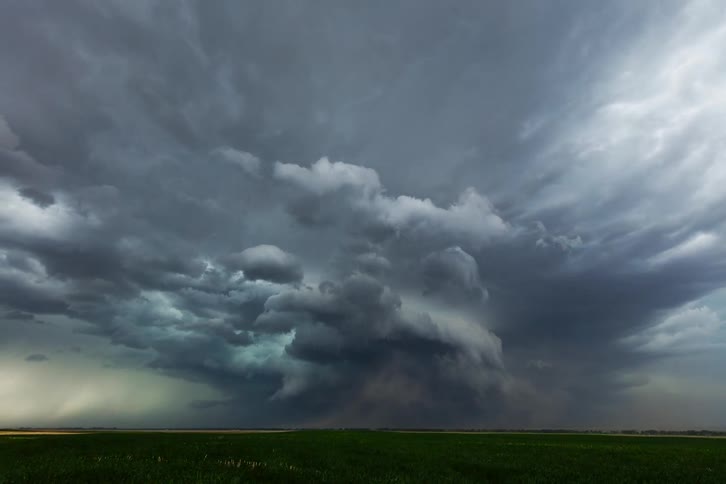 A large dark storm cloud forms over a green field the cloud takes on a funnellike shape as it grows and becomes darker