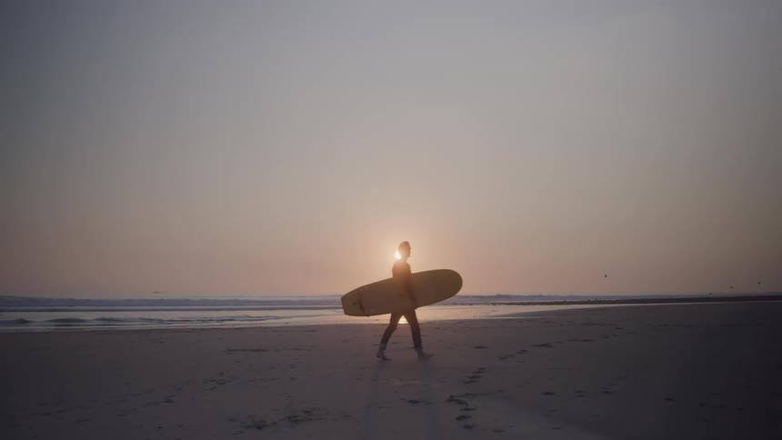 The man walks across the beach with his surfboard