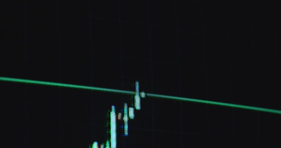 Pixelated macro close-up of a digital screen showing the user interface of an online trading platform or finance app or broker application displaying a candlestick chart or graph with green candles as the price increases and goes up with a positive trend