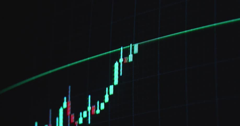 Computer screen shows financial candlestick trading chart consisting of glowing neon green and red candles with wicks as prices goes up with positive trend and little volatility while the stock asset or ETF increases in value over time as good investment