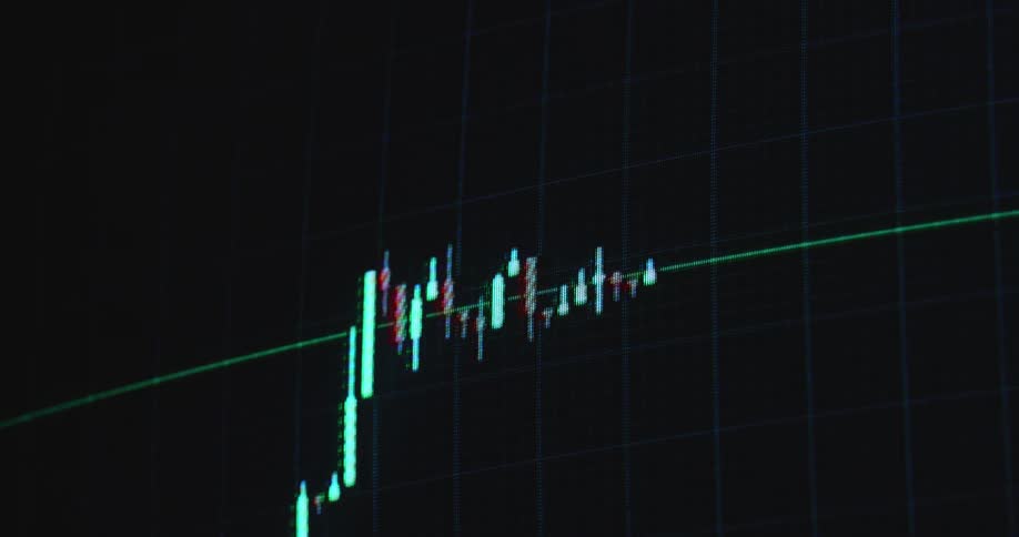 A bullish bull flag chart pattern is displayed on a dark monitor as the red and green candlestick candles form sideways consolidation before breaking resistance for a massive move to the upside with positive price development and profit in a bull run