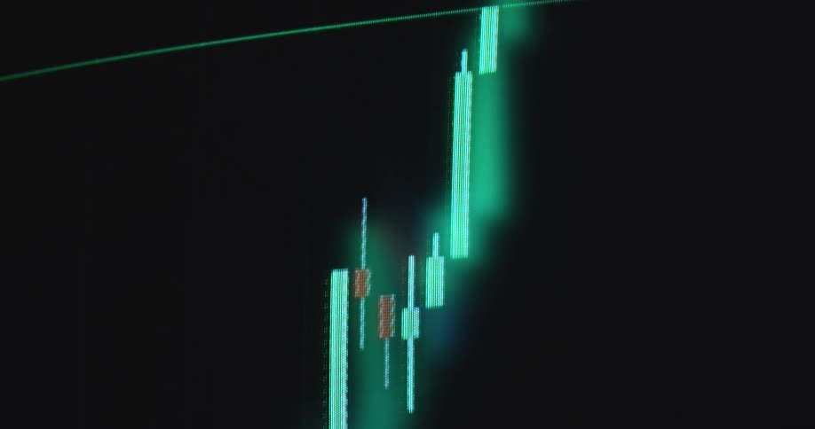 Retro Macintosh computer screen displaying financial market chart of an online trading platform or broker application for buying stocks or shares with bright neon green candles as the price goes up or increases with a positive trend