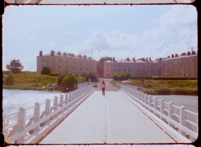 A woman walks down a bridge towards a large building