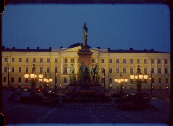 The statue of alexander ii in front of the government palace with cars passing along the road at night in the city