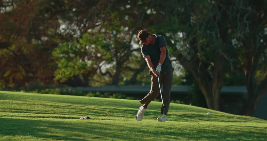 A man swinging to hit a golf ball on a golf course at midday