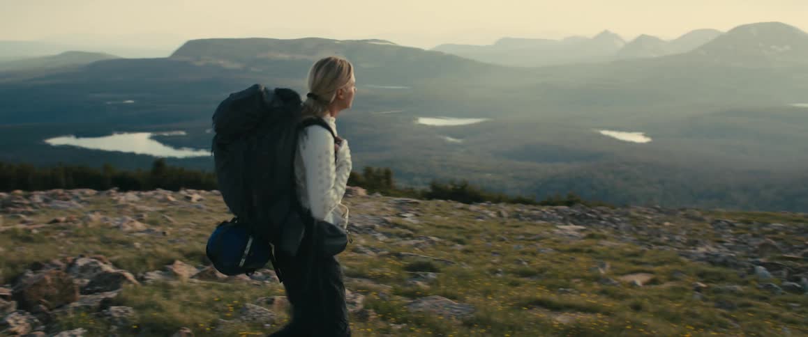 A woman hikes through a rocky mountain landscape carrying a large backpack