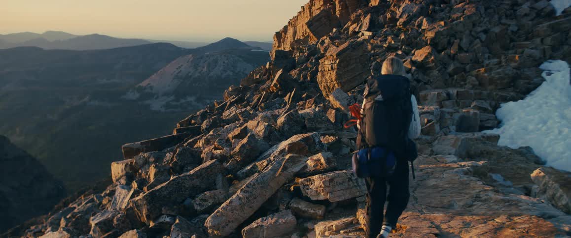 A hiker with a backpack climbs along a rocky mountain ridge at sunset