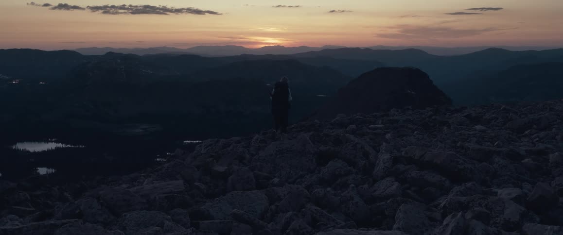 A person hikes through a very rocky mountain range at dusk