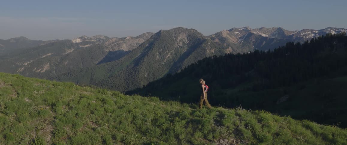 A person walks along a mountain ridge with a landscape of mountains in the background