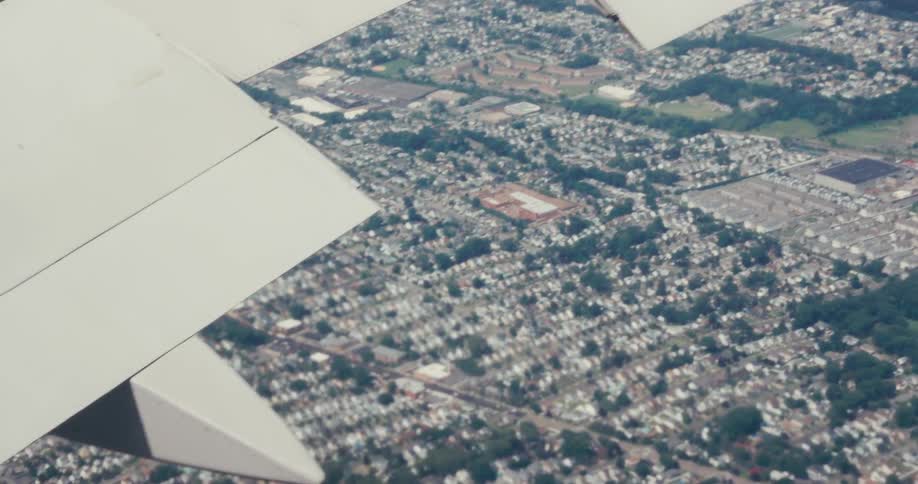 Aerial view of an airplane wing in midflight with a city in the background
