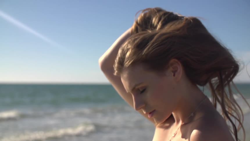 Woman standing on the beach and adjusting her hair