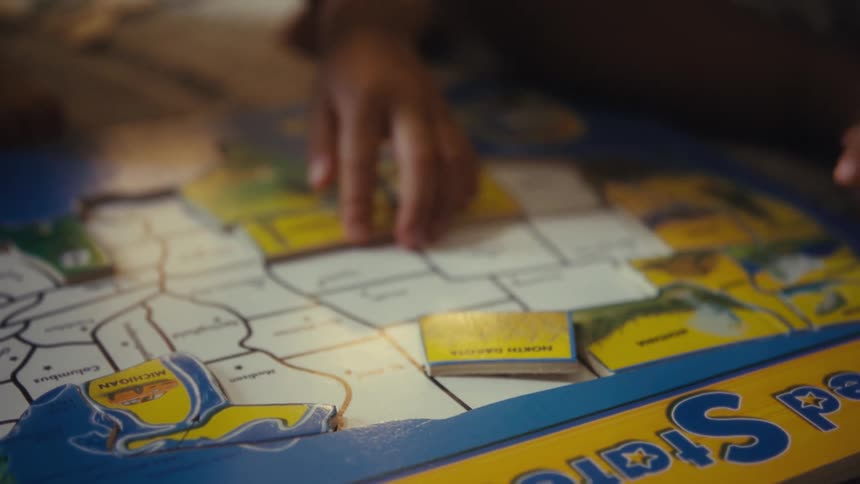 Hands of two toddlers playing indoors with a puzzle in the shape of a map