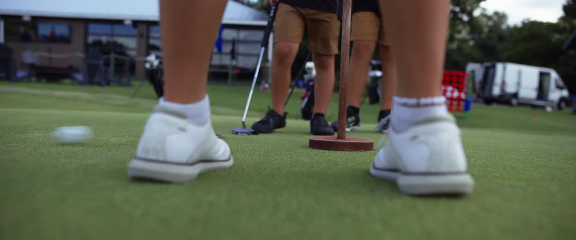Legs of people on a field playing golf