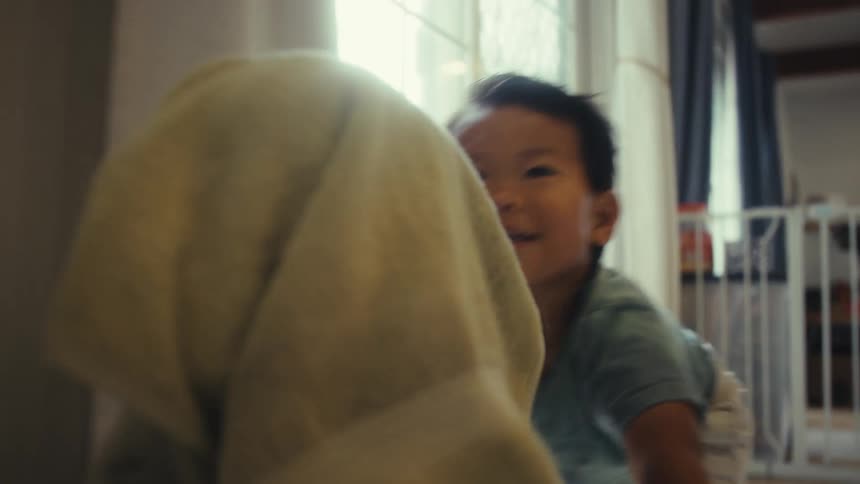 Baby brother pushing sister in laundry hamper as she laughs covering her head with a towel