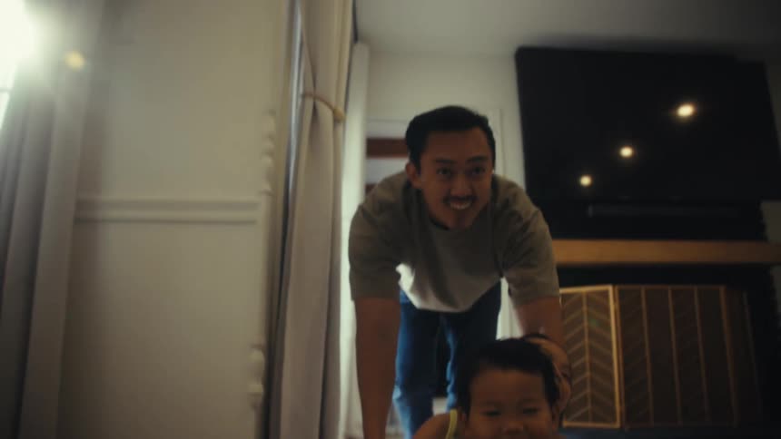 Father playing with his two young children who are in a laundry basket being slid down the hallway of the house