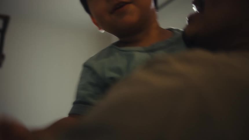 A smiling father holds his laughing young child as they play and bounce around in a room with a window behind them