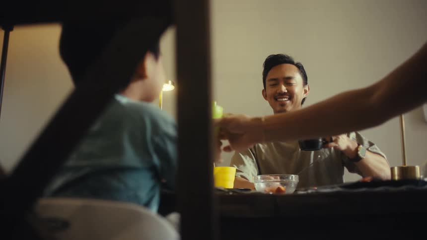 Father and son toasting with cups during a meal at the table