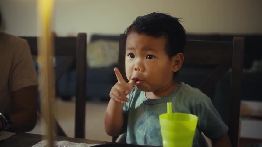 Child sitting at the table sucks their finger while looking curious