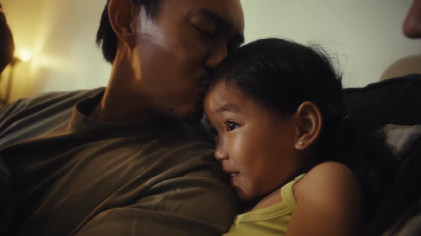 Father kissing his children while sitting next to his wife on the couch