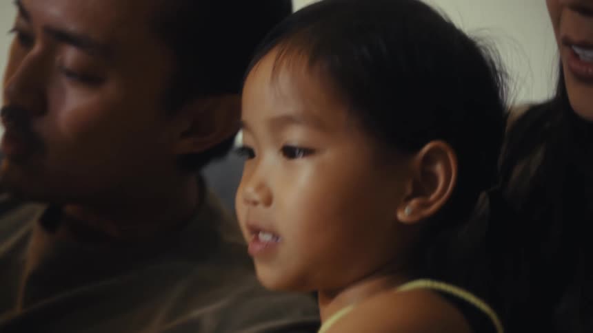 The video shows a family of four including a mother father and two young children sitting on a couch the father is holding a childrens book titled allies fairy the camera zooms in on the little girl who is captivated by the story and then smile