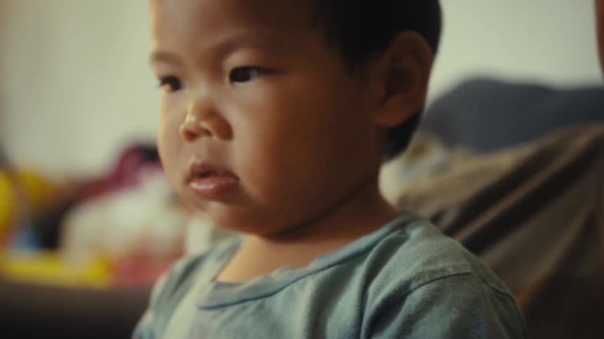 A young girl sits beside a toddler boy indoors with a lamp next to them softly illuminating the room