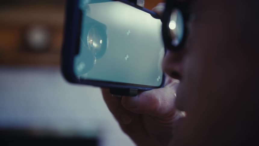 A person holds a smartphone with a lens to their eye while their face and hand are visible