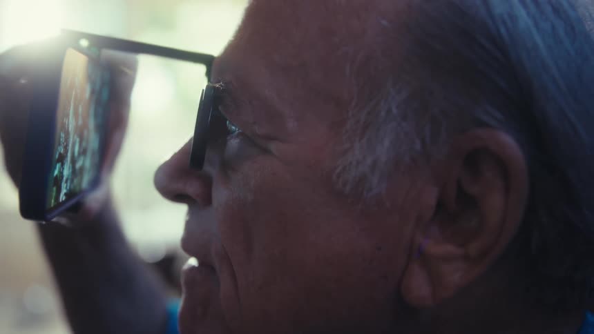 The man is using a cell phone with glasses attached to it