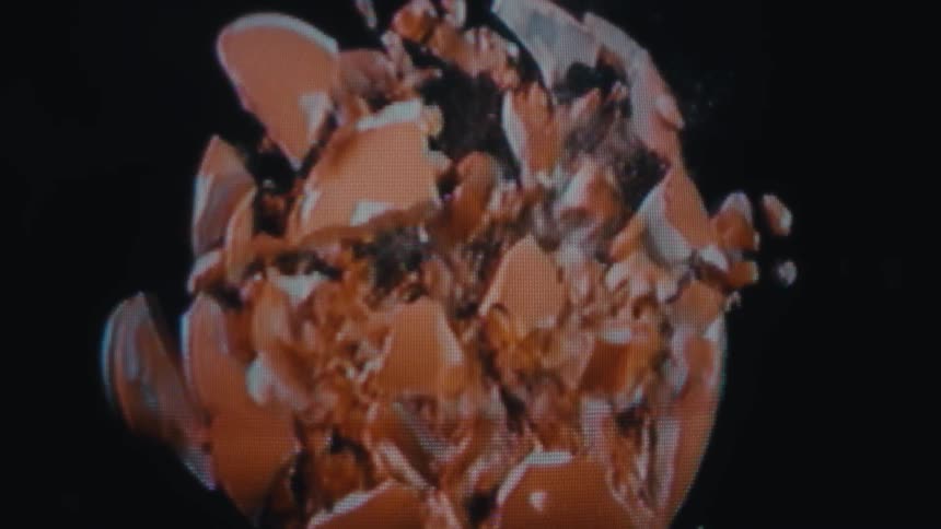 A piggy bank is shown from the back centered on a black background cracks spread across its surface and the piggy bank shatters into many small pieces