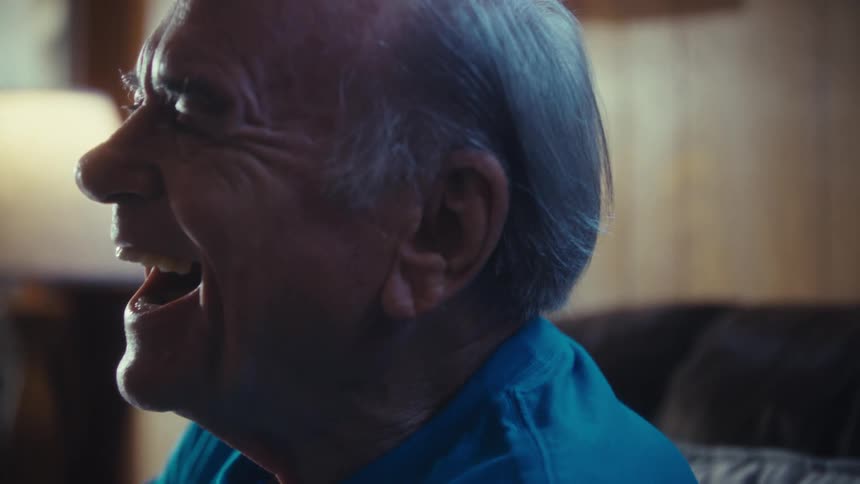 A man with a receding hairline and a watch on his wrist sits in a room and laughs while clap hands