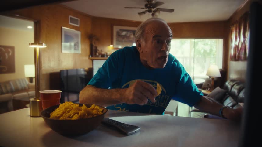 The man eats chips and watches the television