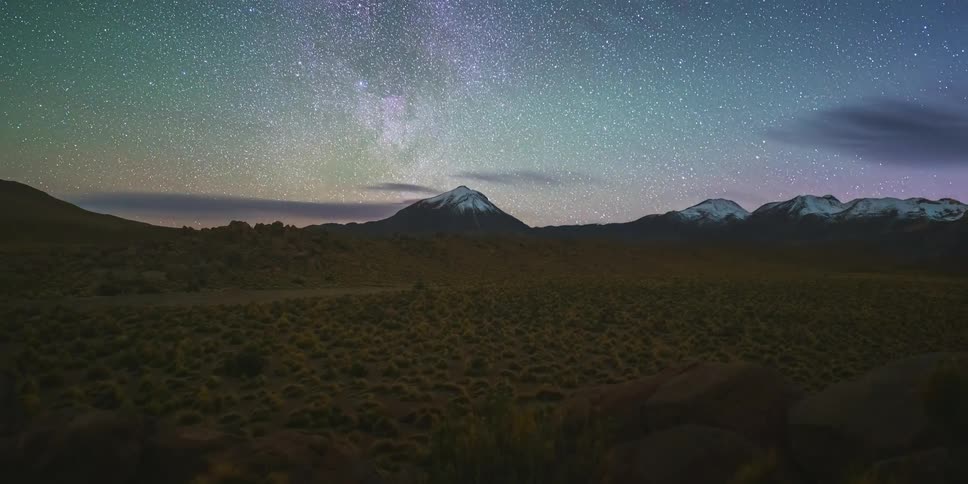 A desert landscape with mountains in the background and a starry sky as night turns into day