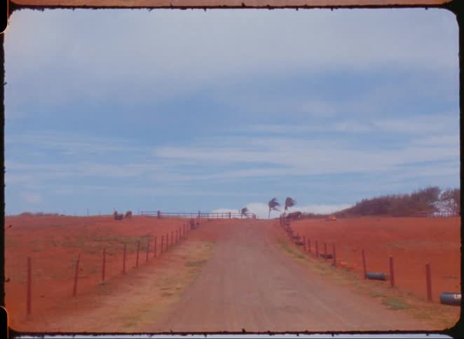 An unpaved road with a fence on each side goes up a hill towards the horizon